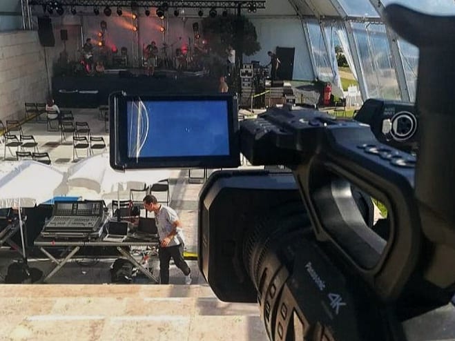 Câmara em primeiro plano, de ecrã aberto, apontada a um palco de concerto com a mesa de som em baixo.